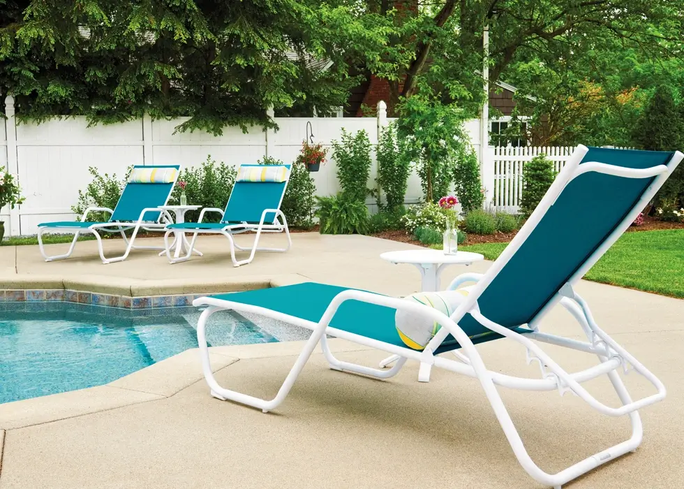 Resort-style pool deck featuring teal sling chaise lounges and side tables designed for comfortable commercial poolside seating.